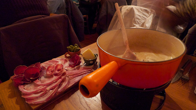 slices of meat sitting next to a pot of cheese fondue
