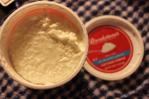 Opened tub of Breakstone's cottage cheese showing its lumpy curds, the red lid beside it