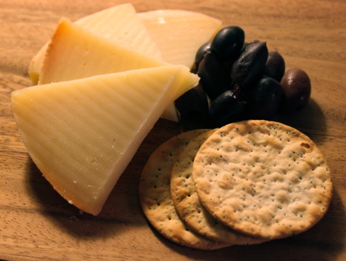 Wedges of Paški sir, Croatian sheep's milk cheese, with black olives and water crackers on a wooden board